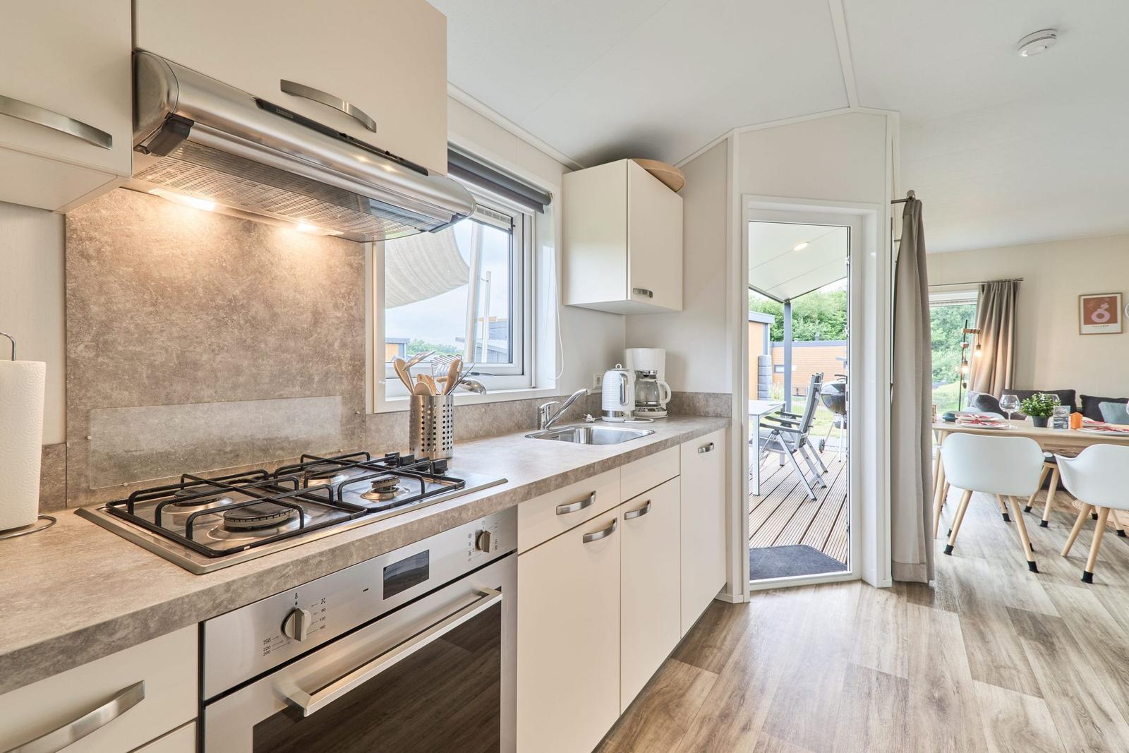 Küche mit Herd, Spüle und Fenster. Durchgang zur Terrasse und Essbereich.