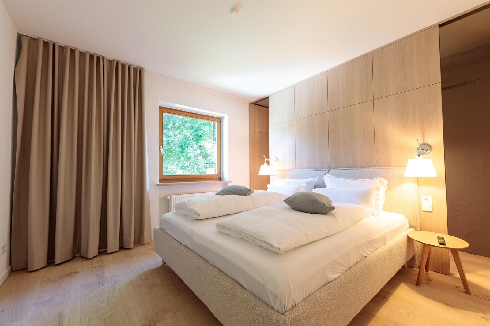 Schlafzimmer mit Doppelbett, Holzfußboden und Fenster mit Blick auf Bäume.