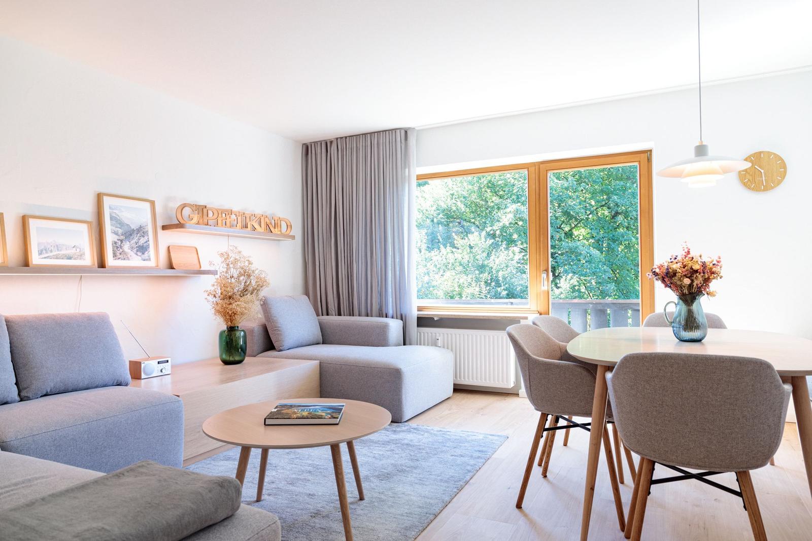 Wohn- und Essbereich mit Sofa, Tisch und Blick auf grüne Bäume.