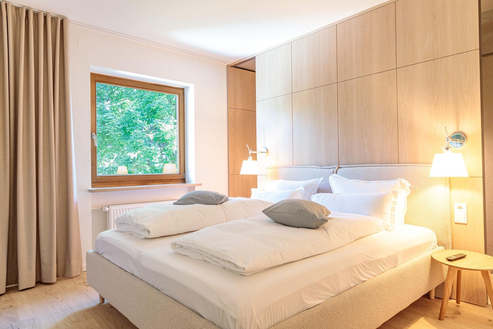 Schlafzimmer mit Doppelbett, Holzwand und Fenster mit Blick auf Bäume.