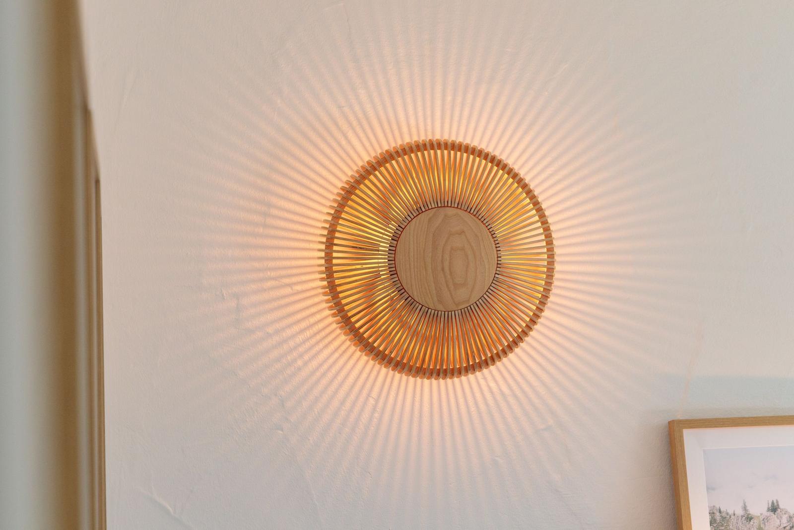 Wandlampe mit Holzrahmen und Strahlenmuster an der Wand.