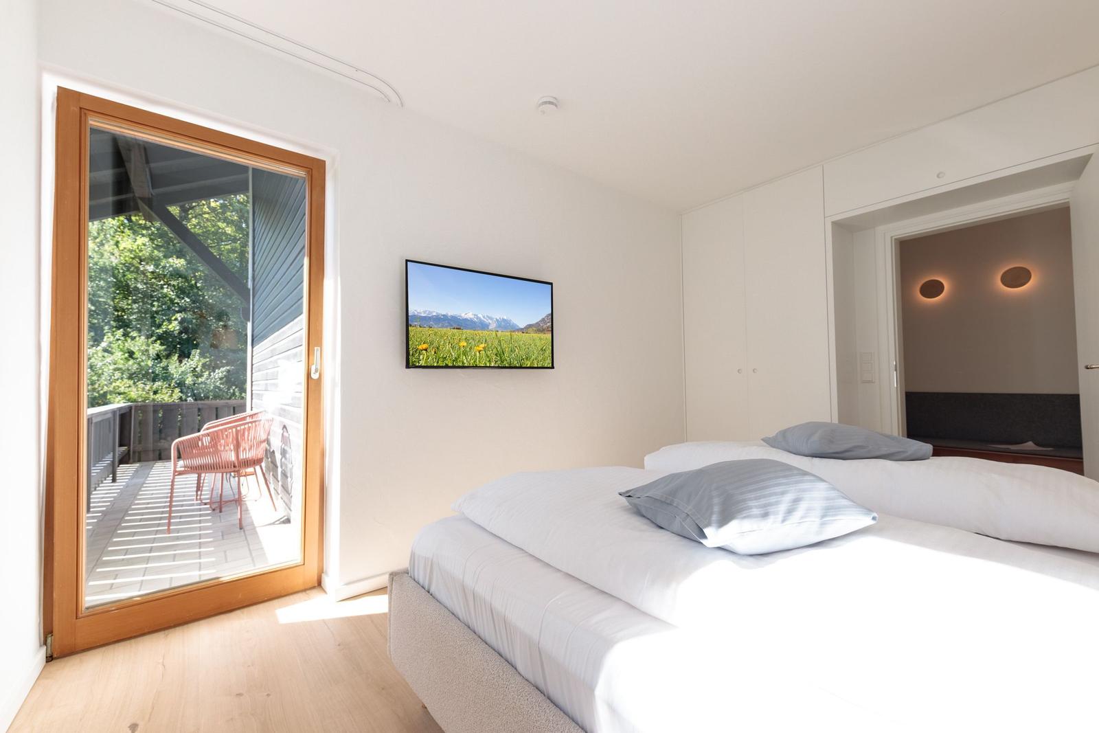 Schlafzimmer mit Bett, TV und Balkonzugang.