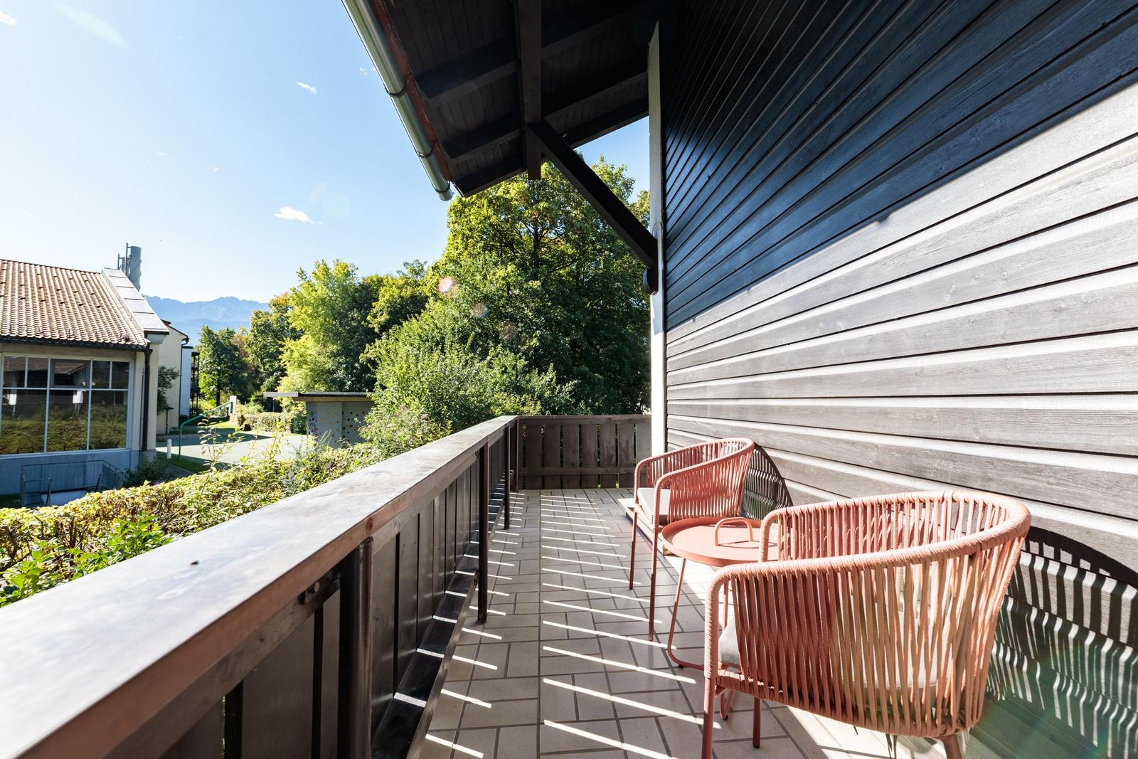 Terrasse mit zwei Stühlen und Tisch, Blick auf grüne Bäume und Gebäude.