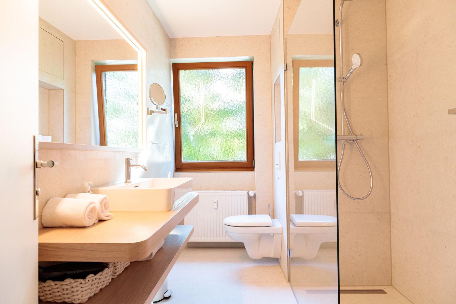 Badezimmer mit Dusche, Waschbecken und Toilette. Fenster mit Blick auf Grün.