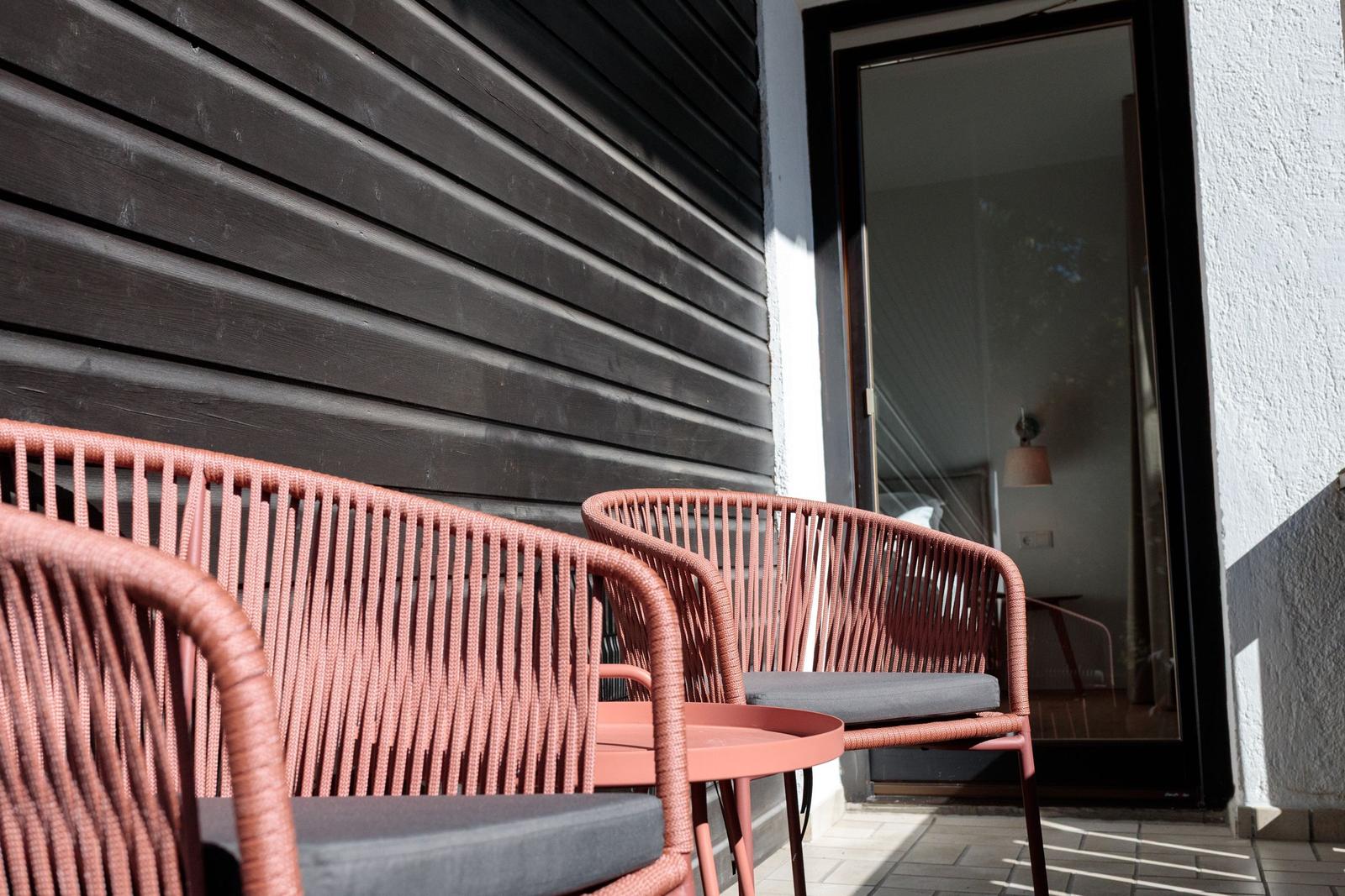 Terrasse mit zwei Stühlen und Tisch. Durch Glastür ist Schlafzimmer sichtbar.