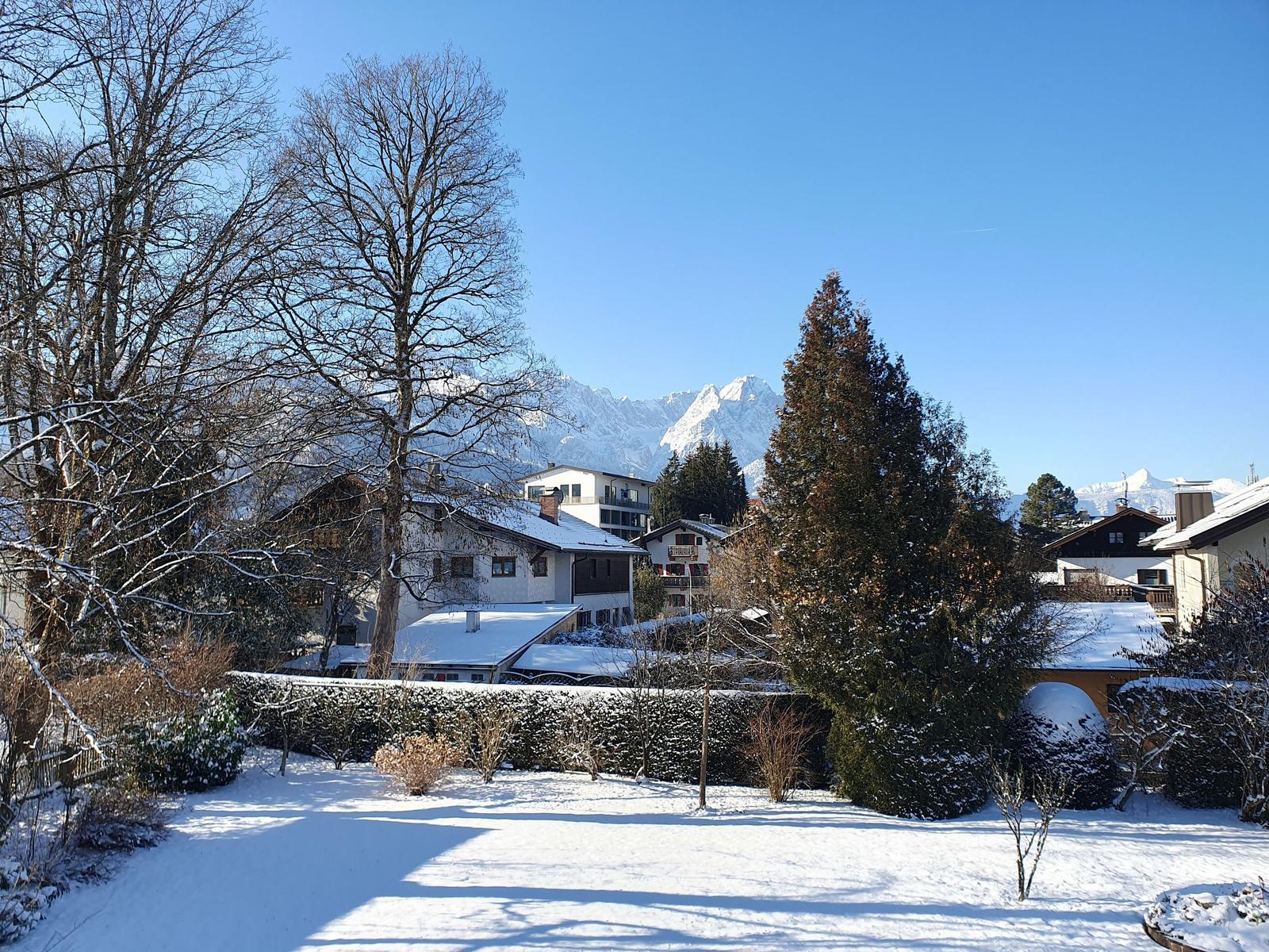 Schneebedeckter Garten mit Blick auf schneebedeckte Berge und Häuser.