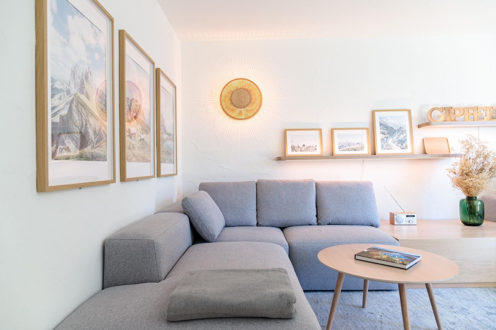 Ein Wohnzimmer mit grauem Sofa, Holztisch und Wandbildern.