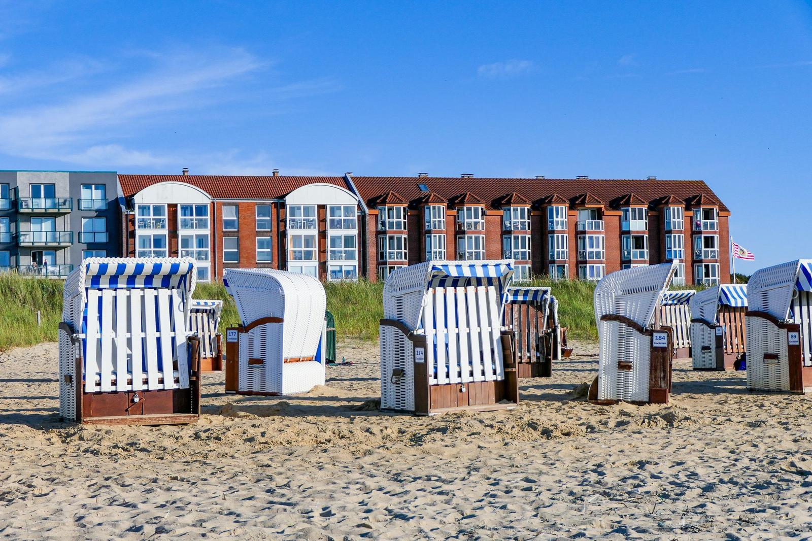 Strand mit Liegestühlen und Ferienhaus im Hintergrund.
