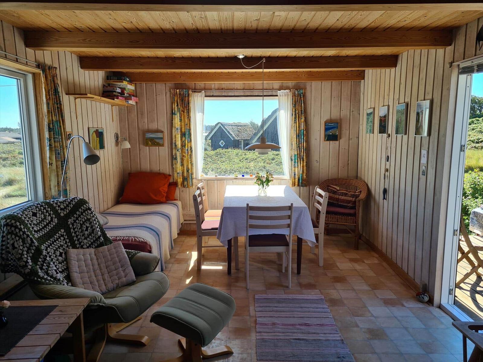 Living space with dining table, bed, and seating. Wooden walls and large windows.