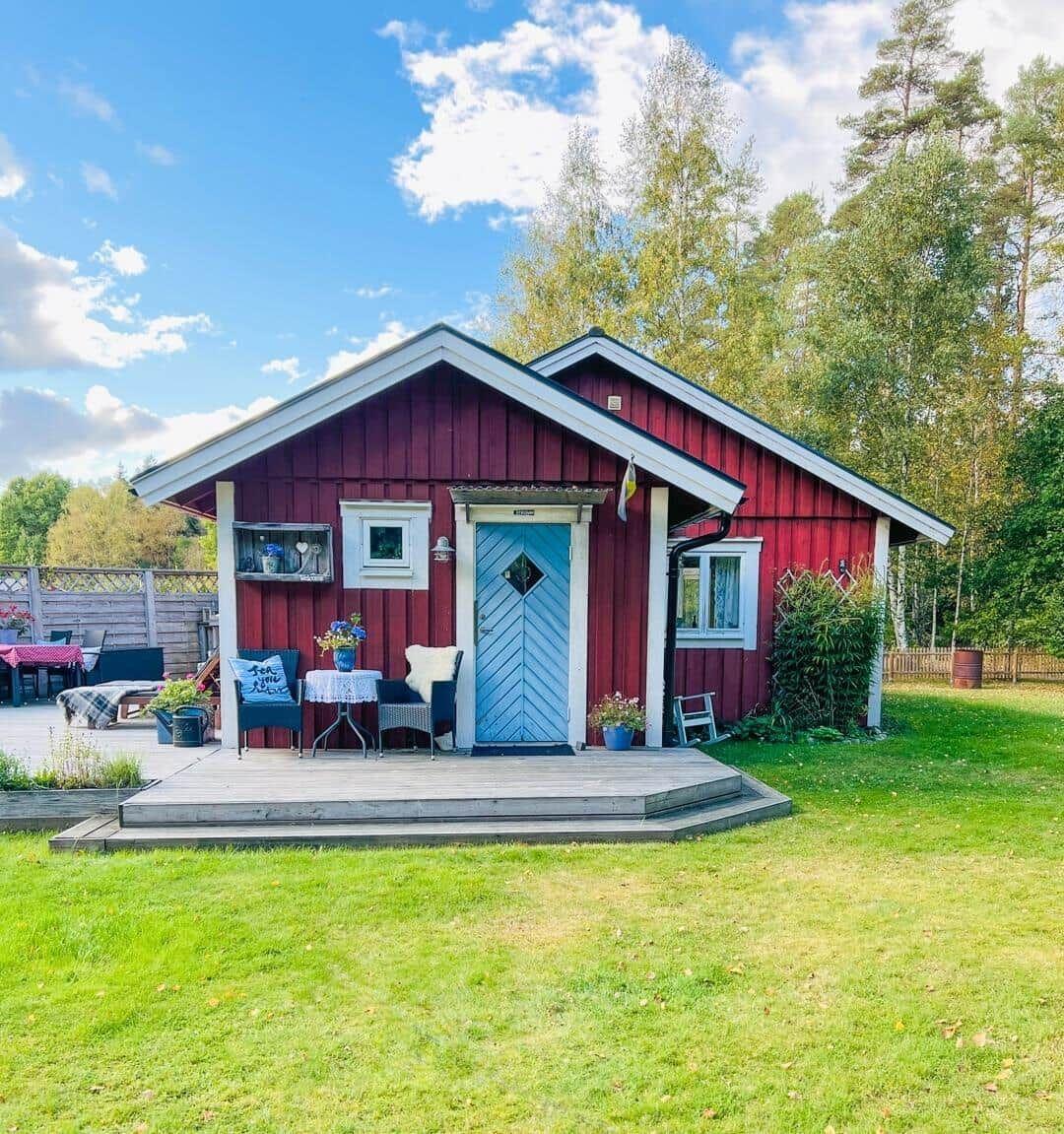 Rotes Holzhaus mit blauer Tür und Terrasse im Grünen.