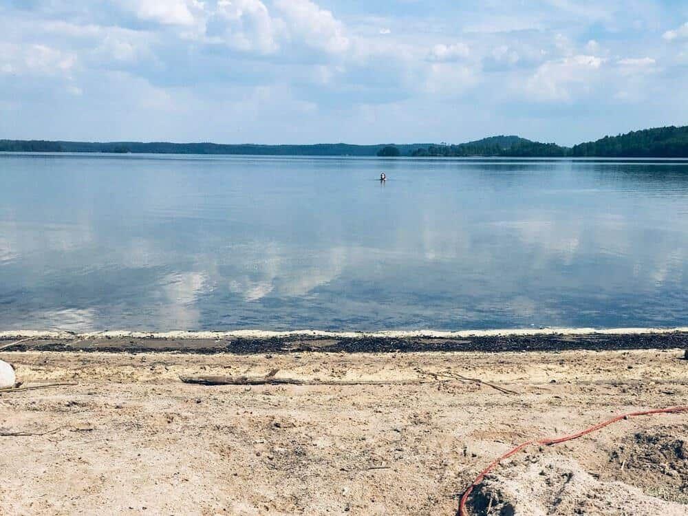 Ein ruhiger See mit Sandstrand und einem Boot im Wasser.