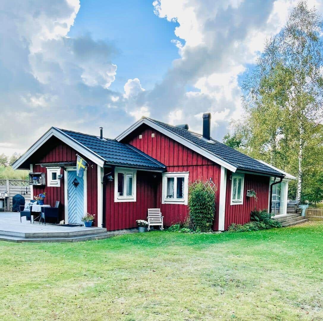 Rotes Holzhaus mit Terrasse und Garten unter blauem Himmel.