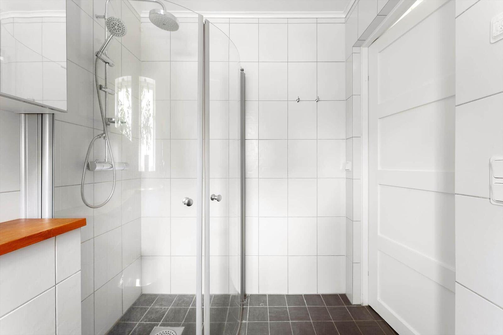 Dusche mit Glaswand, weißen Fliesen und dunklem Boden