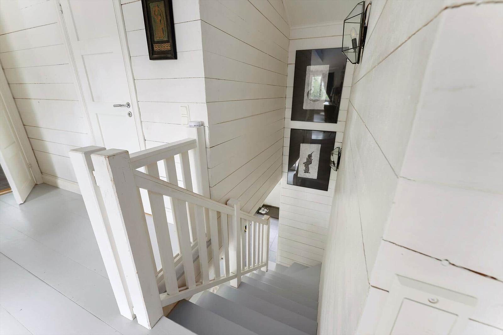 Helle Treppe mit weißem Geländer und Holzwänden. Wandbilder und Deckenleuchte sichtbar.