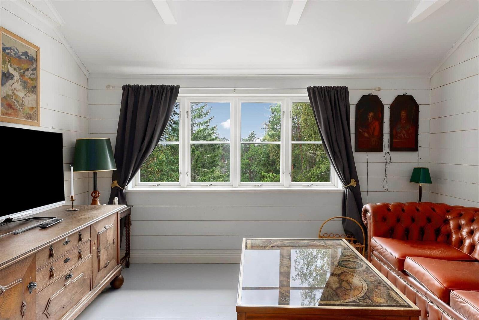 Wohnzimmer mit rotem Ledersofa, Glas-Tisch und Fensterblick auf Wald.