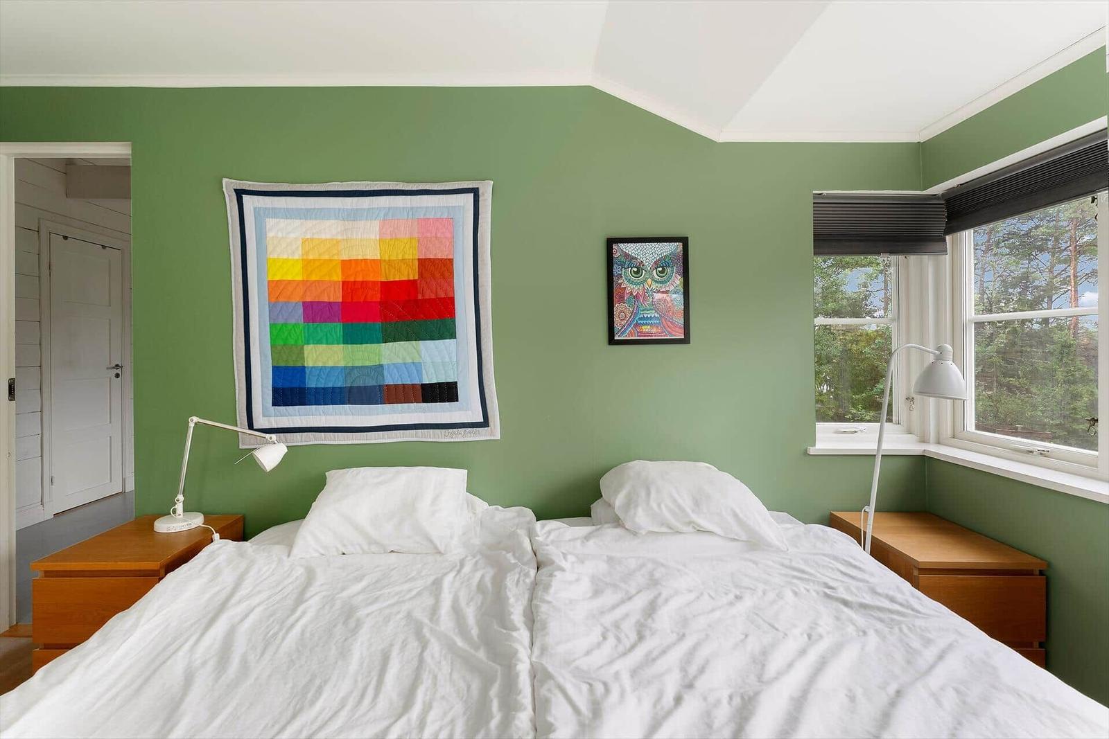 Schlafzimmer mit grünen Wänden, Doppelbett, Fenster und Kunst an der Wand.