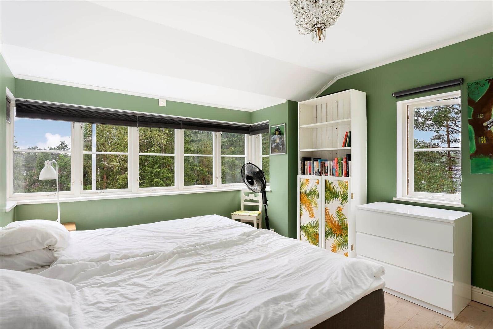 Schlafzimmer mit grünen Wänden, großem Fenster und weißem Bett.