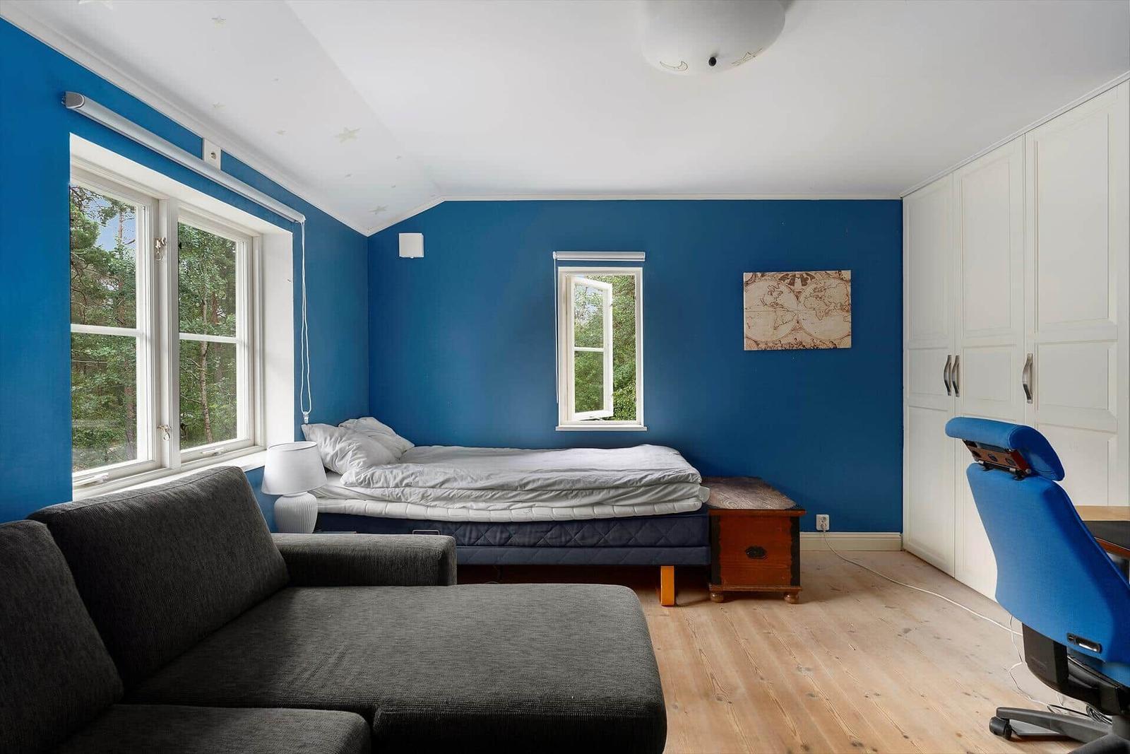 Schlafzimmer mit blauen Wänden, Bett, Sofa und Schreibtischstuhl.