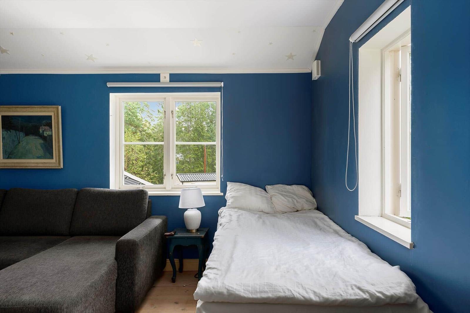 Zimmer mit blauen Wänden, Bett, Sofa und Fenstern.