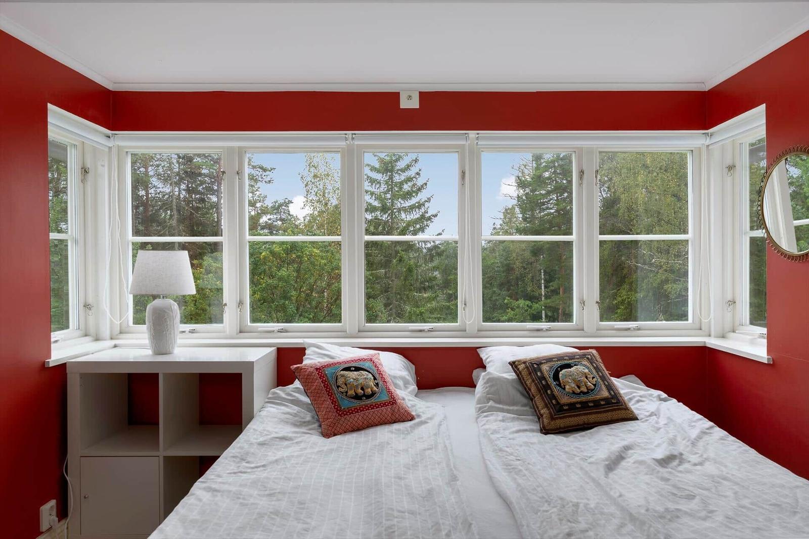 Schlafzimmer mit roten Wänden und großem Fensterblick auf Wald.