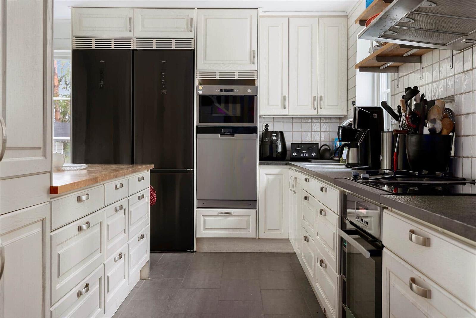 Küche mit weißen Schränken, schwarzer Kühlschrank und moderner Küchenzeile.