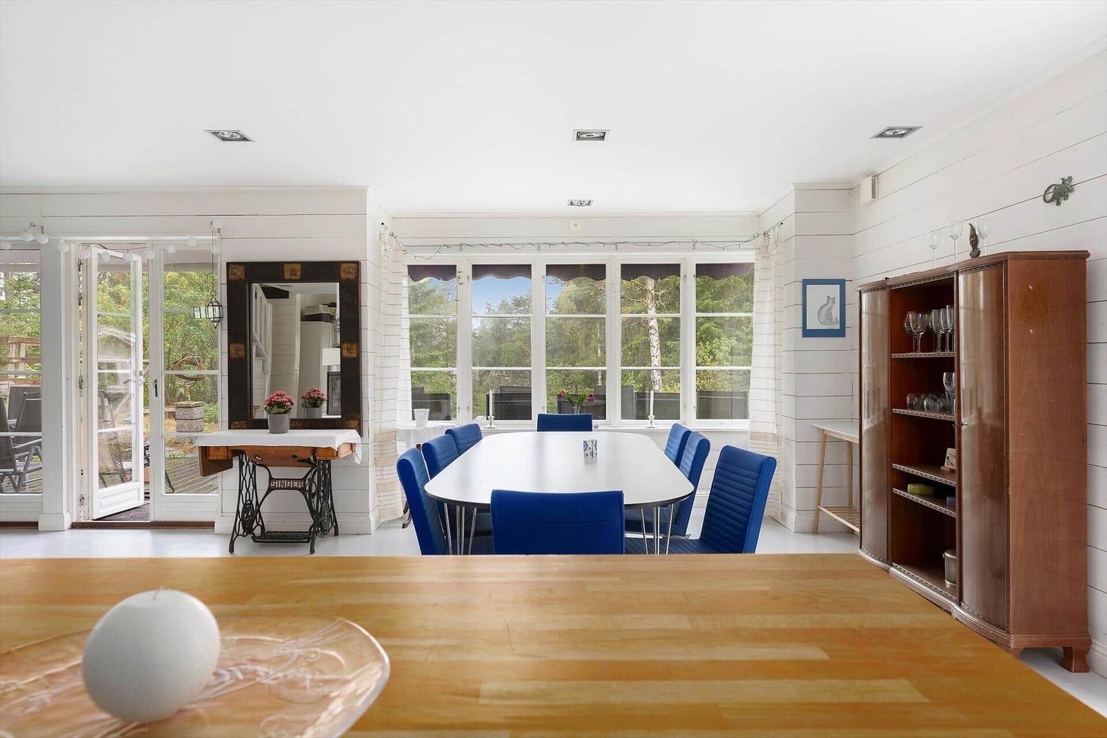 Esszimmer mit blauen Stühlen und großem Fenster. Holztisch im Vordergrund.