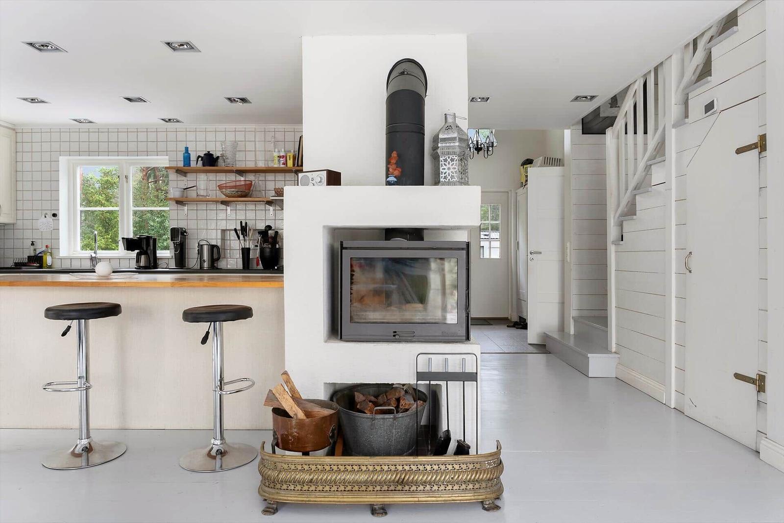 Küche mit Stehplatz, Kaminofen und Holzstapel. Hintergrund: Treppe und Fenster.