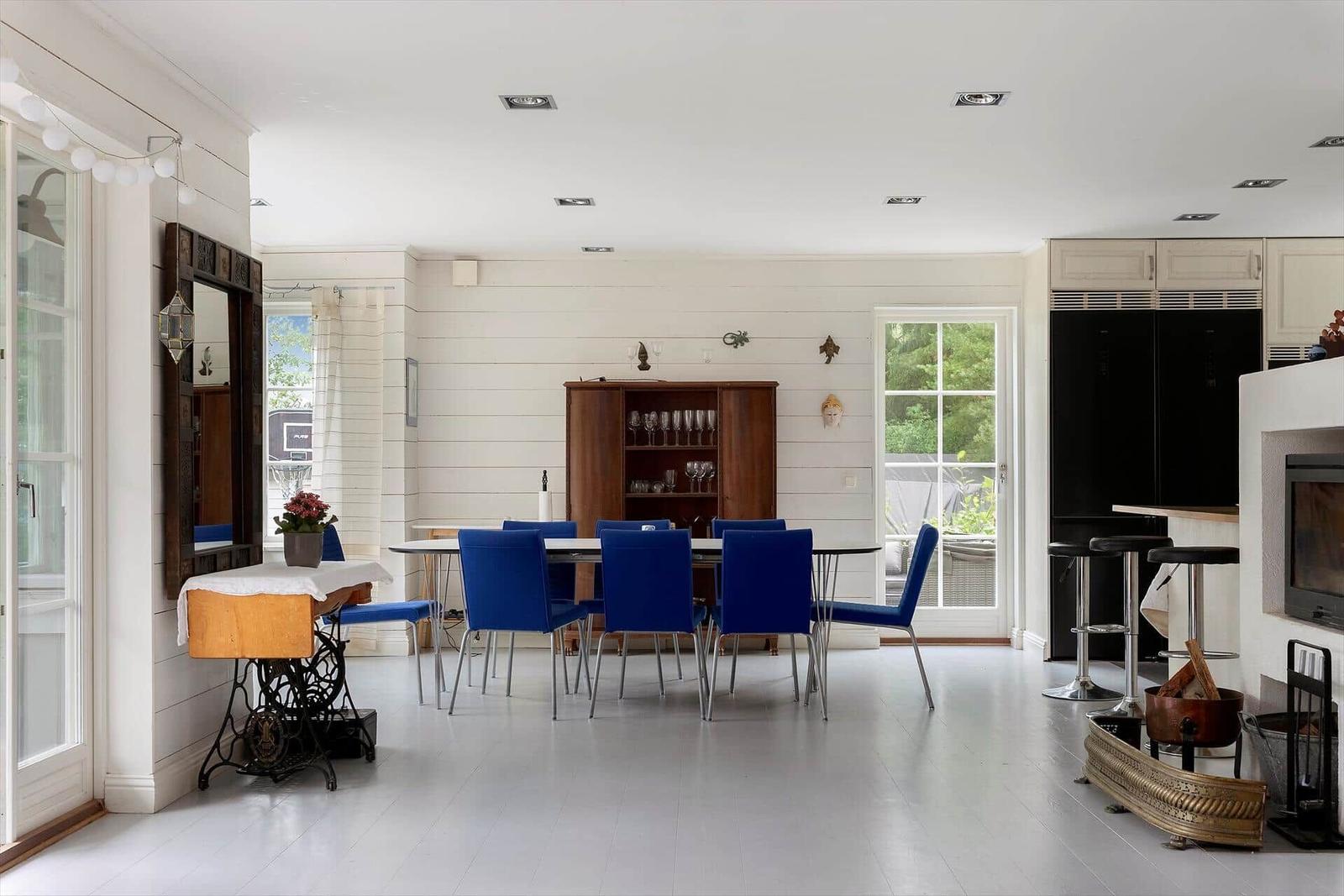 Esszimmer mit blauen Stühlen, Holzschrank und Fenstern zum Garten.