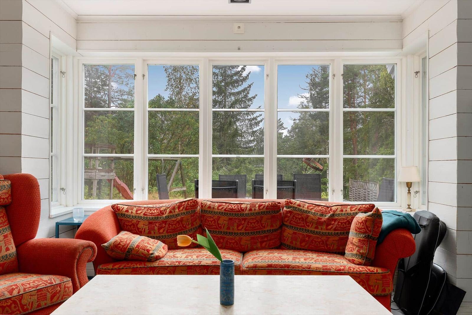 Ein Wohnzimmer mit rotem Sofa und großen Fenstern zum Garten.