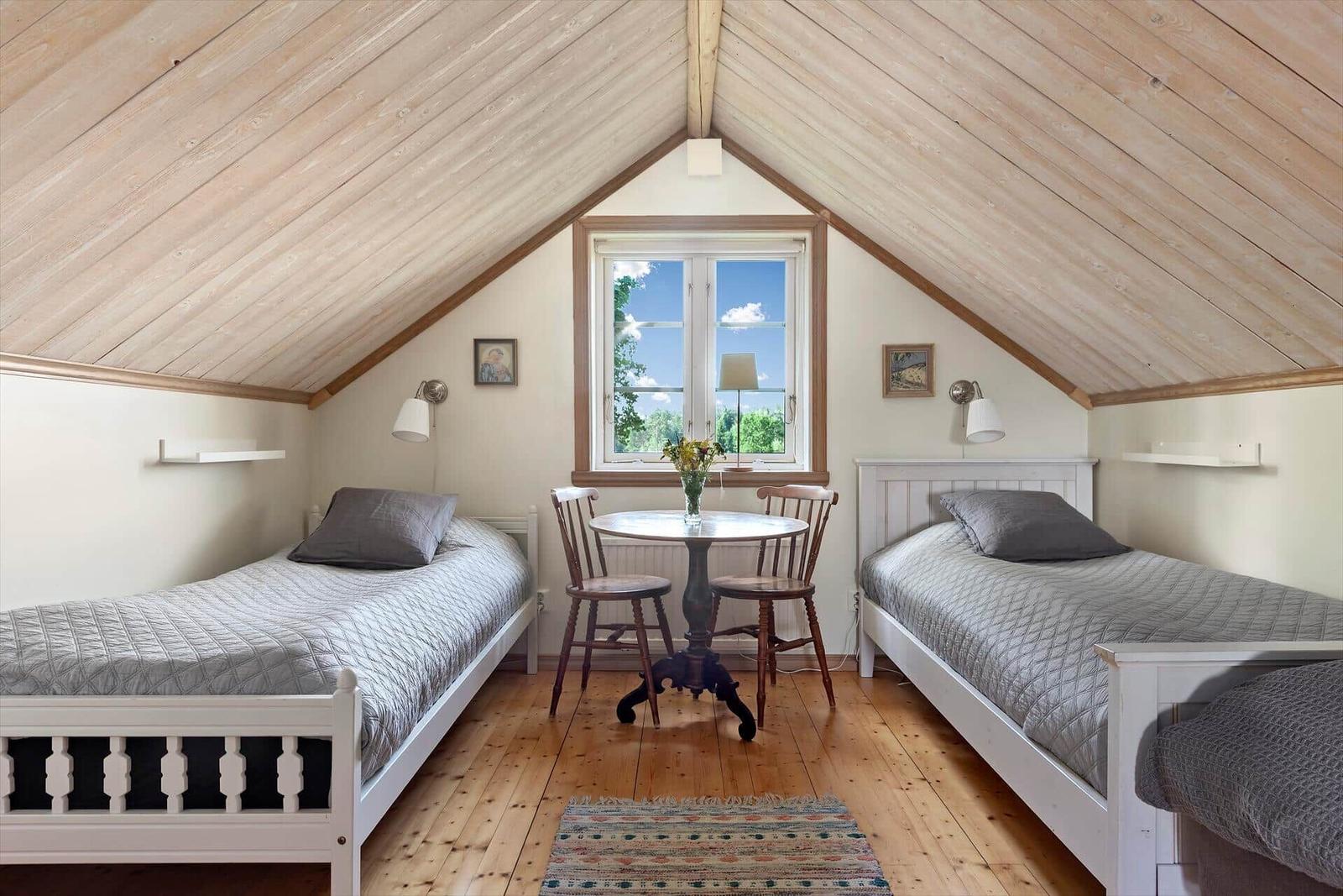 Zwei Betten, Tisch mit Stühlen, Fenster, Holzdecke und Boden.