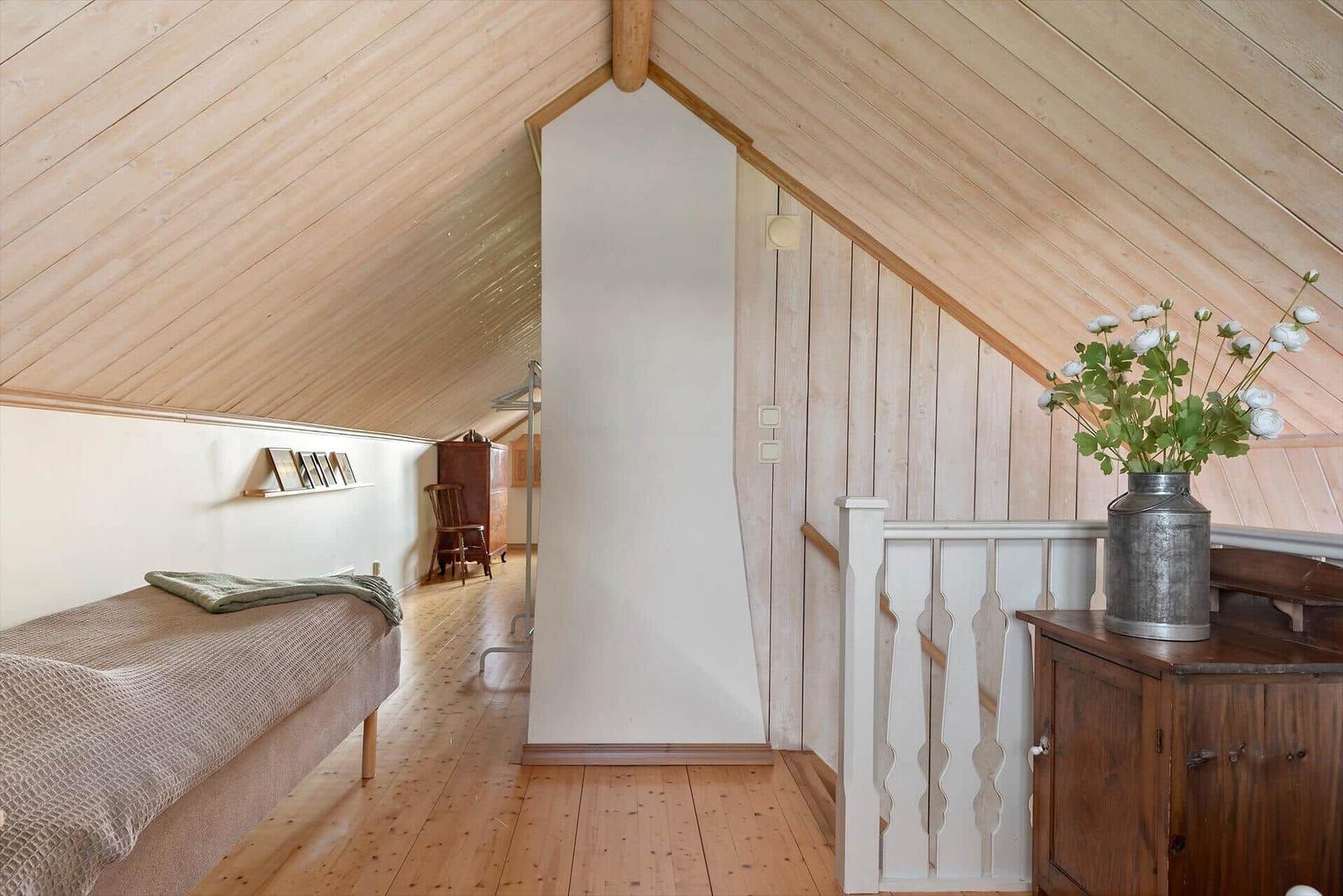 Schlafzimmer mit Holzdecke, Bett, Schrank und Blumen in Metalltopf.