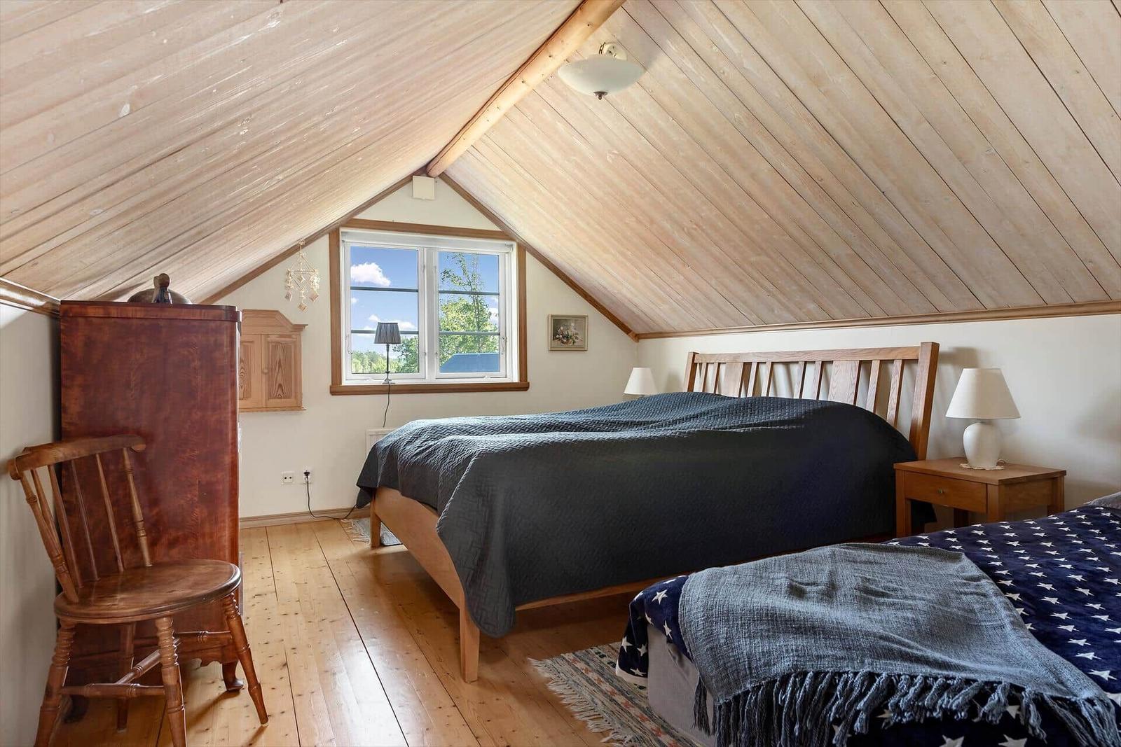 Schlafzimmer mit zwei Betten, Holzdecke und Fenster mit Blick nach draußen.