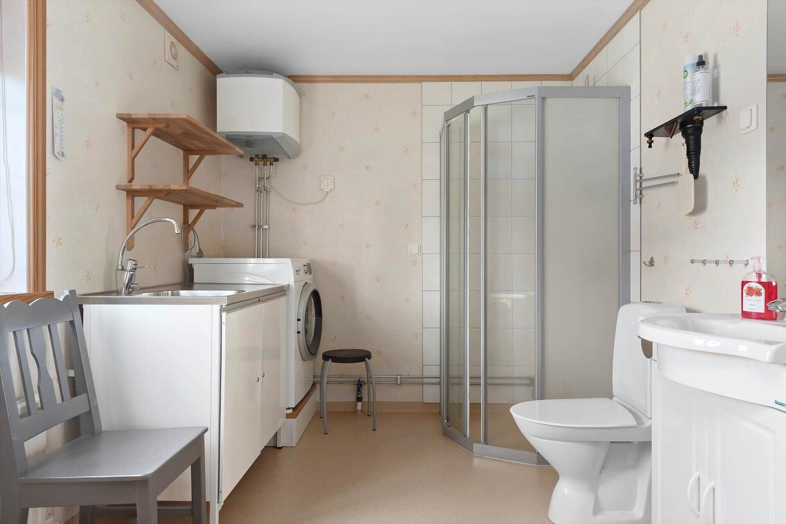 Badezimmer mit Dusche, Toilette, Waschmaschine und Waschbecken.