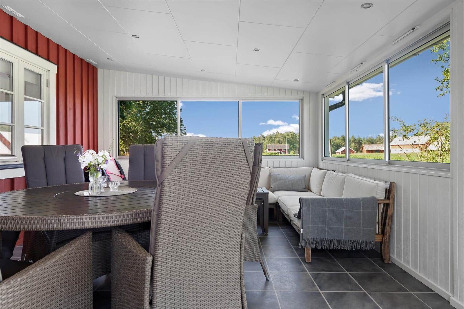 Terrasse mit Sitzgruppe, Tisch und Stühlen. Große Fenster mit Blick auf Landschaft.