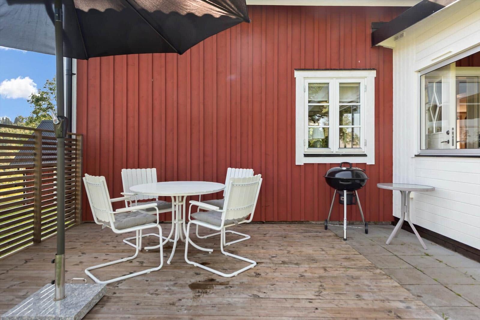 Terrasse mit Tisch, Stühlen, Sonnenschirm und Grill vor rotem Holzhaus