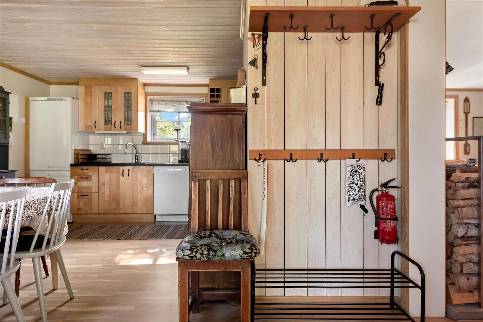 Eingangsbereich mit Kleiderhaken und Feuerlöscher. Küche mit Holzmöbeln und Fenster.