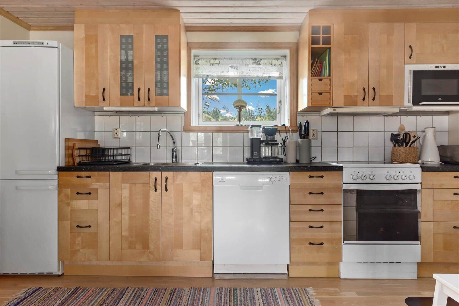 Küche mit Holzschränken, Waschmaschine und Fenster mit Blick.