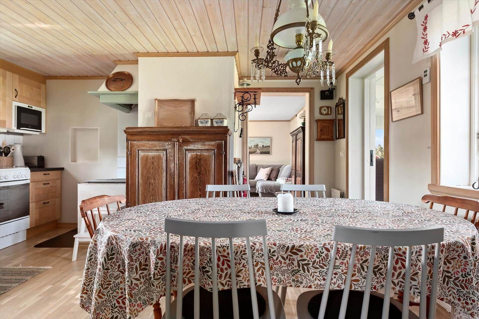 Esszimmer mit runden Tisch, Stühlen und Holzdecke. Küche und Wohnzimmer sind sichtbar.