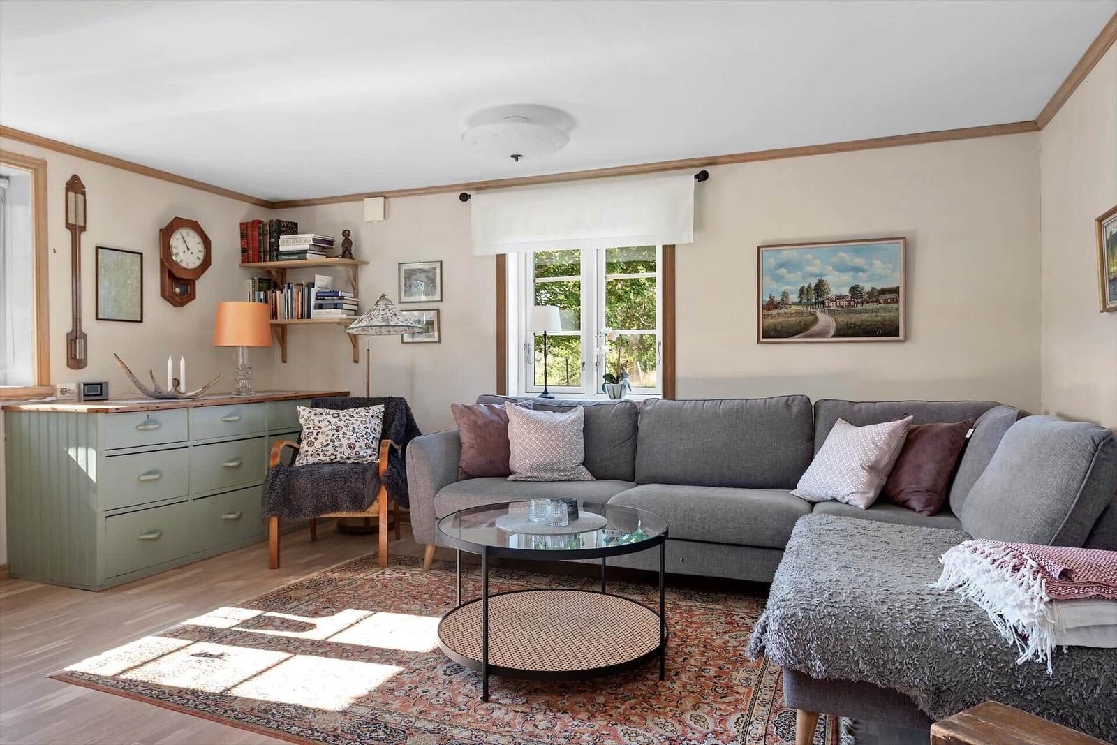 Wohnzimmer mit Sofa, Couchtisch und Wandbildern. Fenster mit Blick auf Grün.