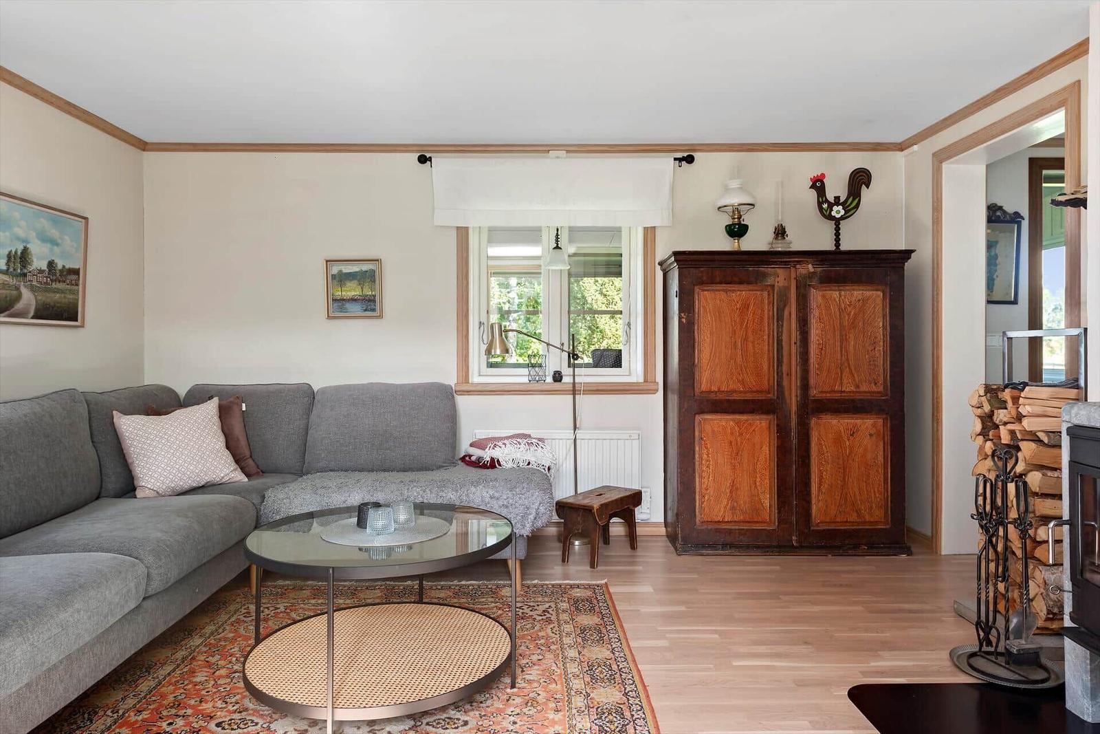 Wohnzimmer mit Sofa, Tisch und Holzschrank. Fenster, Kamin und Holzfußboden.