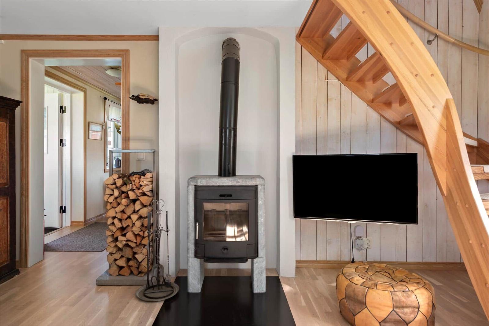 Wohnzimmer mit Kaminofen, Holzstapel und TV an der Wand.