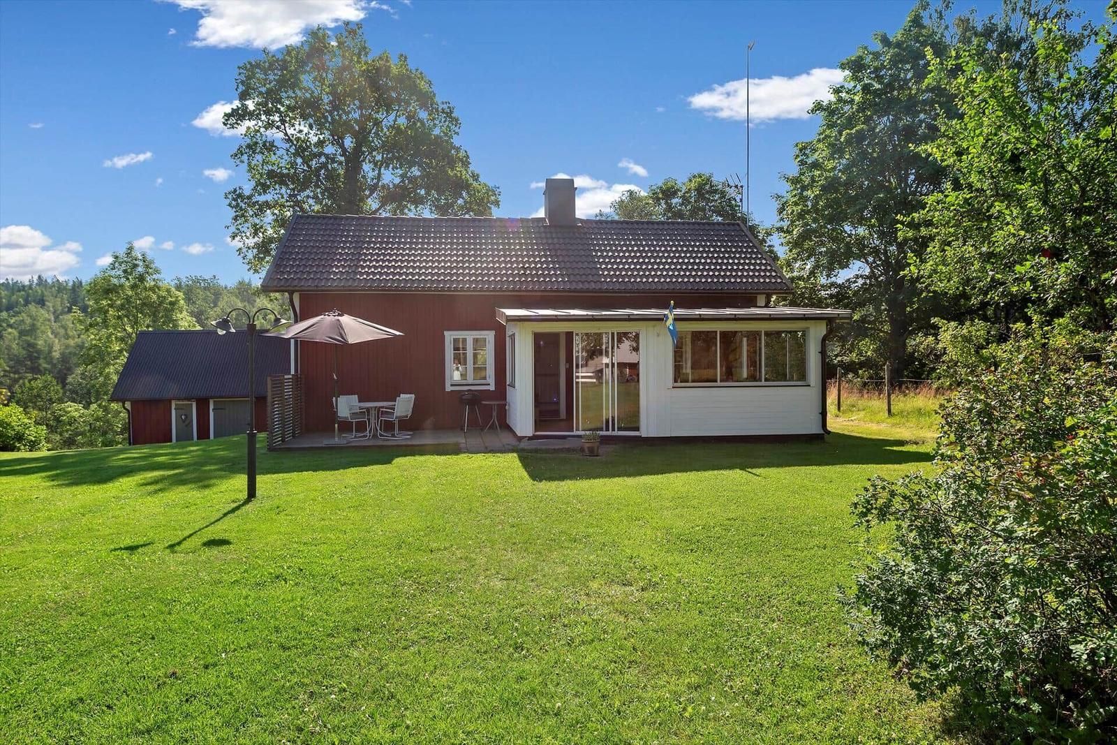 Rotes Haus mit weißem Anbau, Garten und Terrasse mit Sonnenschirm.