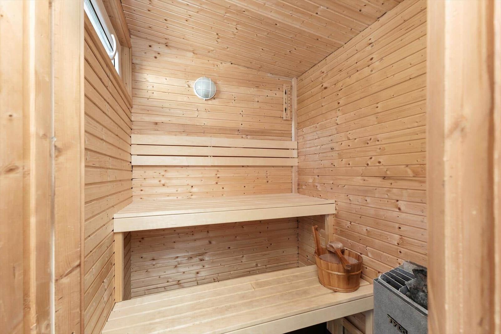 Sauna mit Holzbank, Holzwand und Holzdecke. Holzschale und Ofen sind vorhanden.