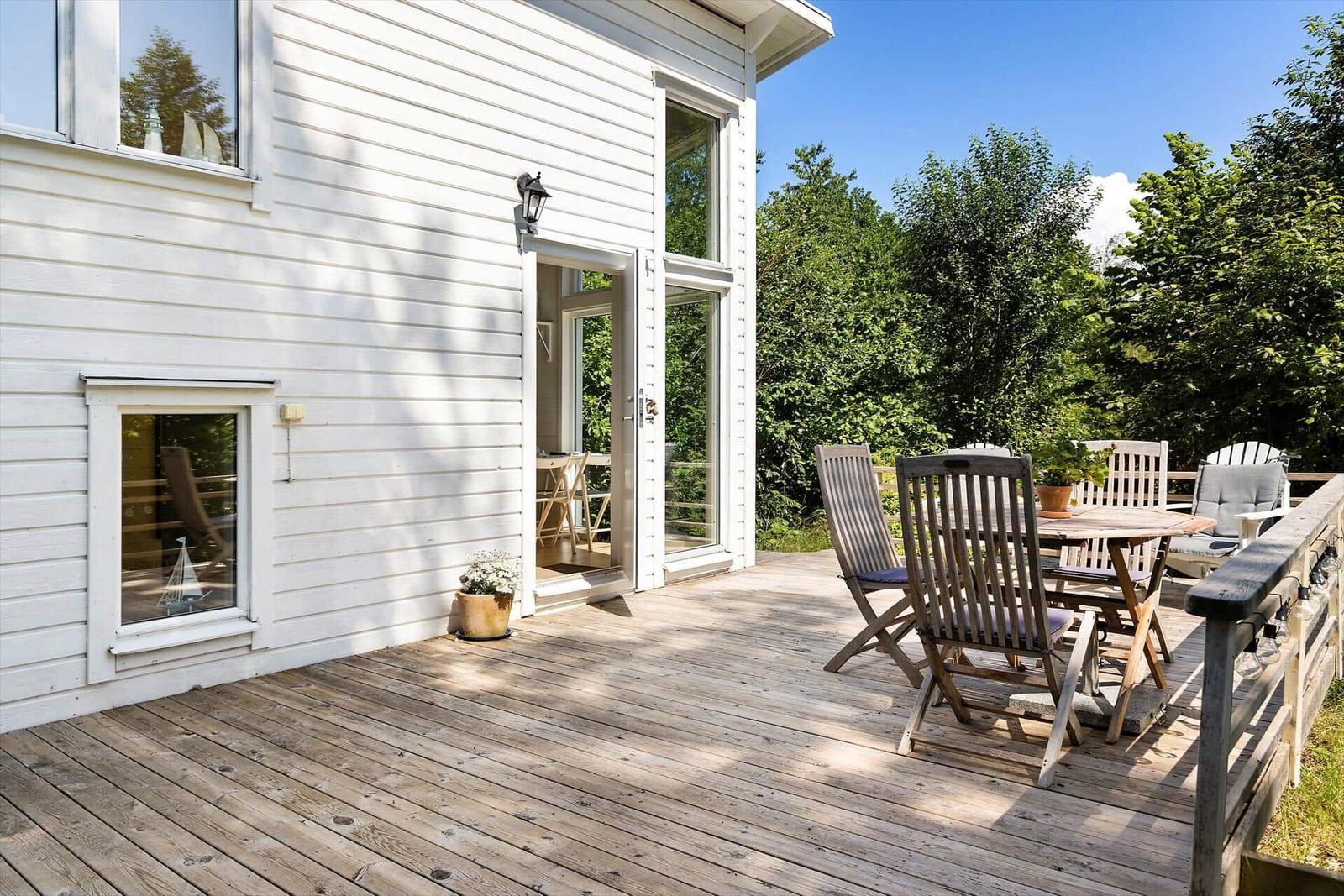 Terrasse mit Holztisch und Stühlen neben weißem Haus mit Fenstern.