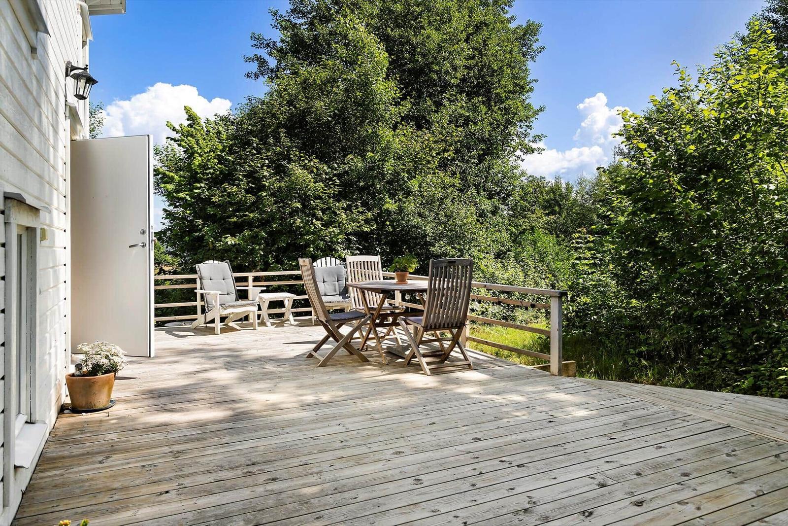 Terrasse mit Tisch, Stühlen und Sicht auf grüne Bäume.