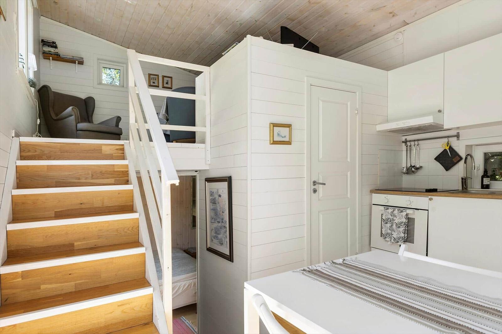 Küche mit Arbeitsplatte, Stufen zum Schlafbereich, weiße Wände und Holzdecke.