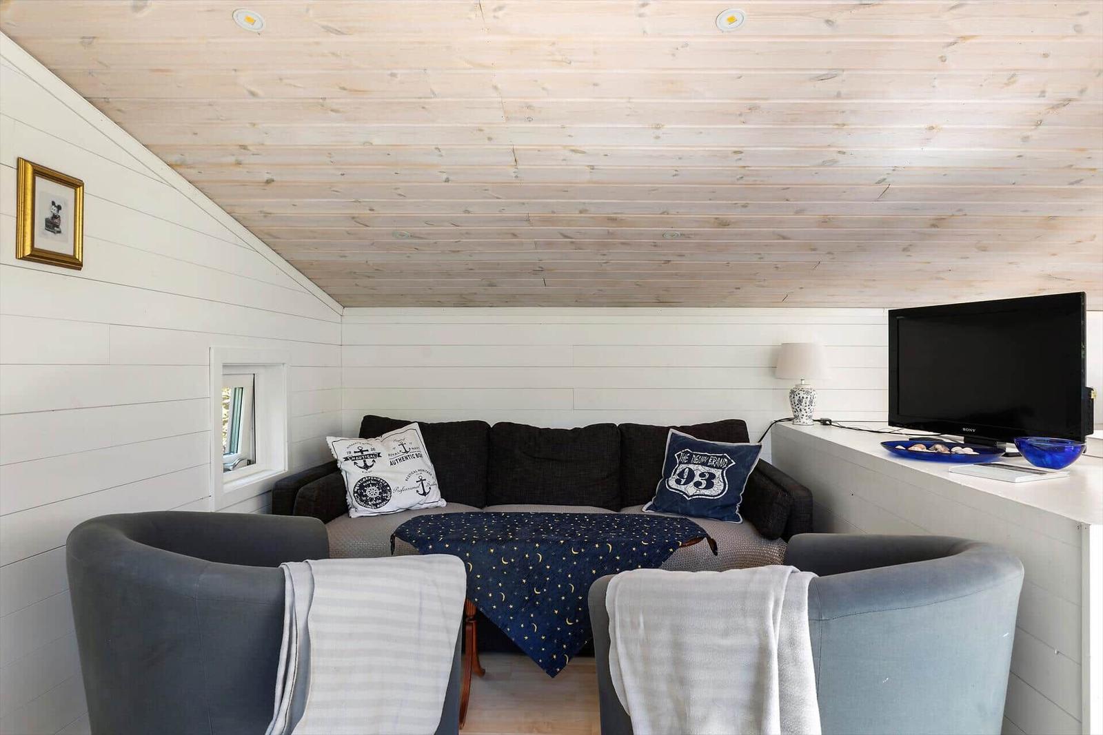 Wohnzimmer mit Sofa, zwei Sesseln und Fernseher an der Wand.