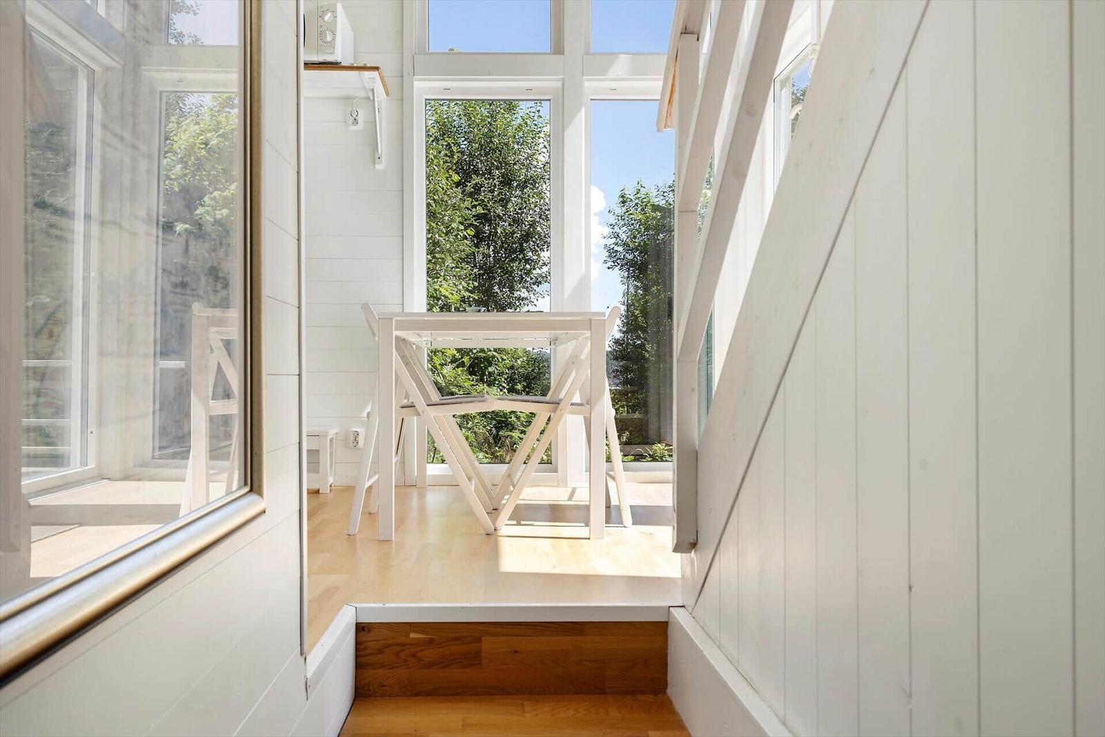 Durchgehendes Fenster mit Tisch und Stühlen. Blick auf grüne Bäume und Himmel.