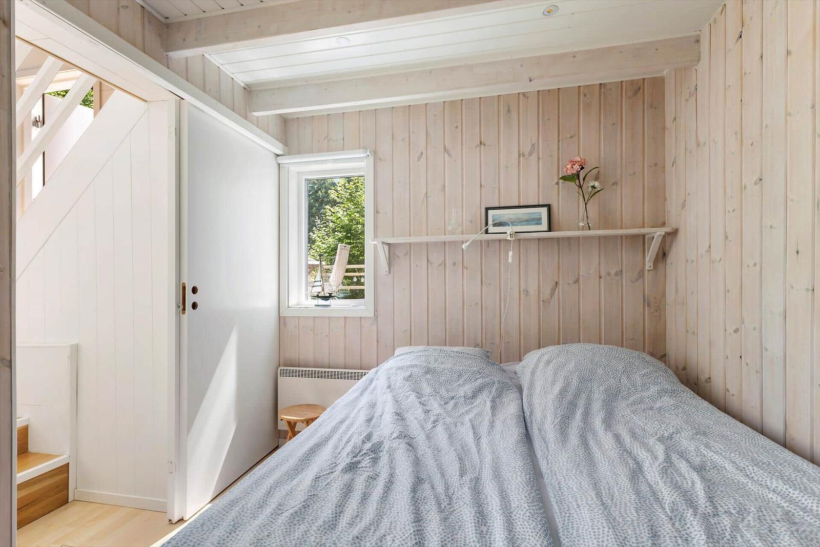 Schlafzimmer mit Holzwand, Bett, Fenster und Schrank.