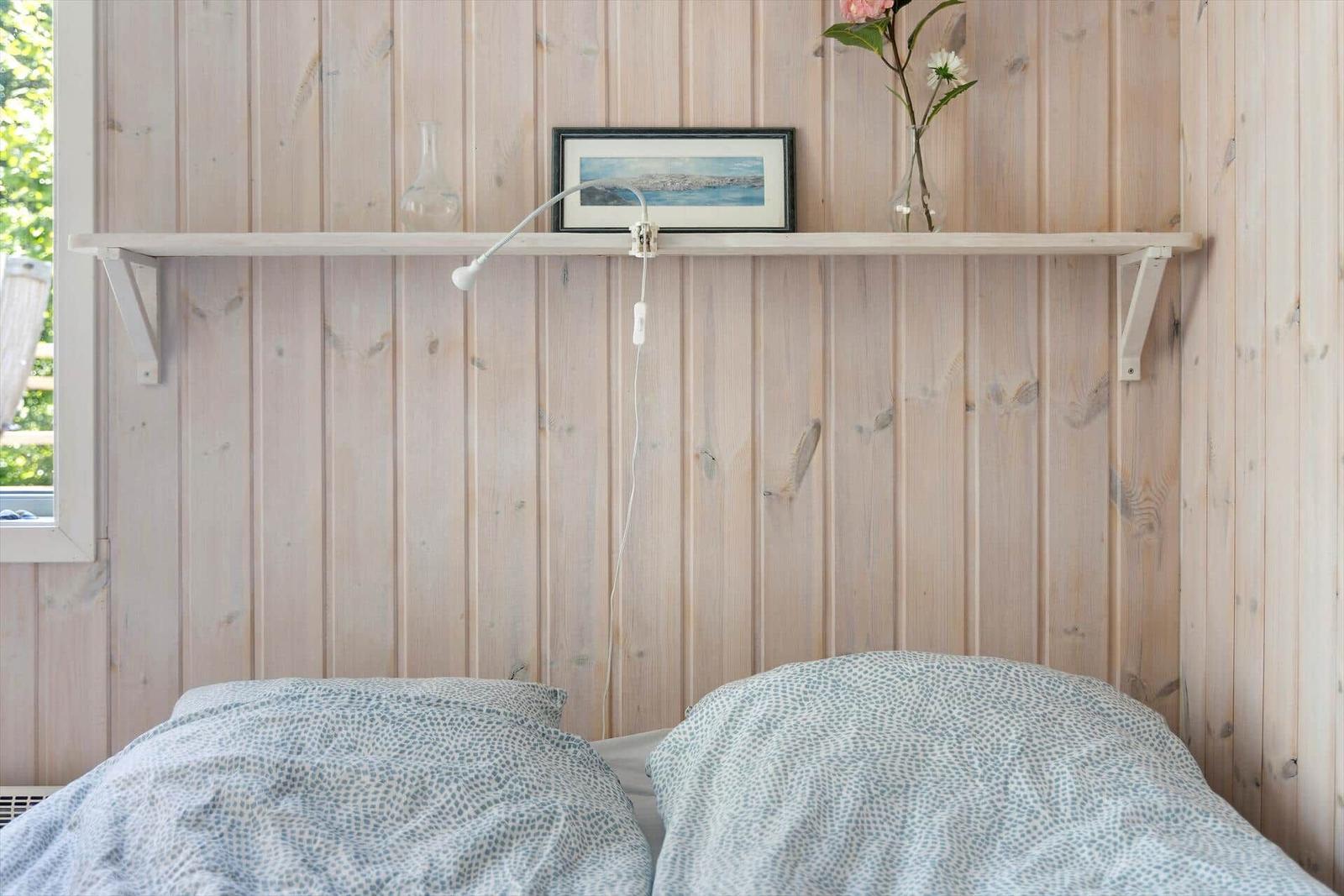 Schlafzimmer mit Holzwand, Bett und Regal mit Bild und Blumen.